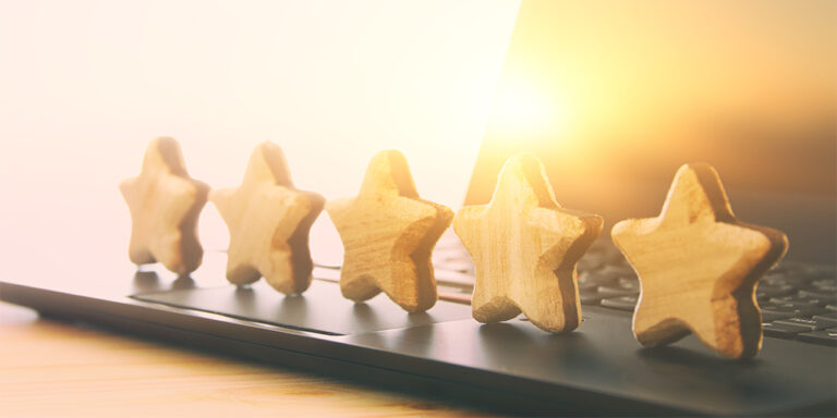 Five wooden star shapes are lined up on a laptop keyboard, sunlight shining in the background—symbolizing a high rating, excellent review, and recognition as a Top 1000 Clutch provider.