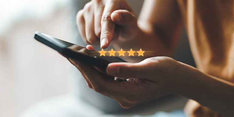 A person’s hand holding a smartphone, using their index finger to select a five-star rating on the screen—representing positive feedback for their preferred direct marketing partner.