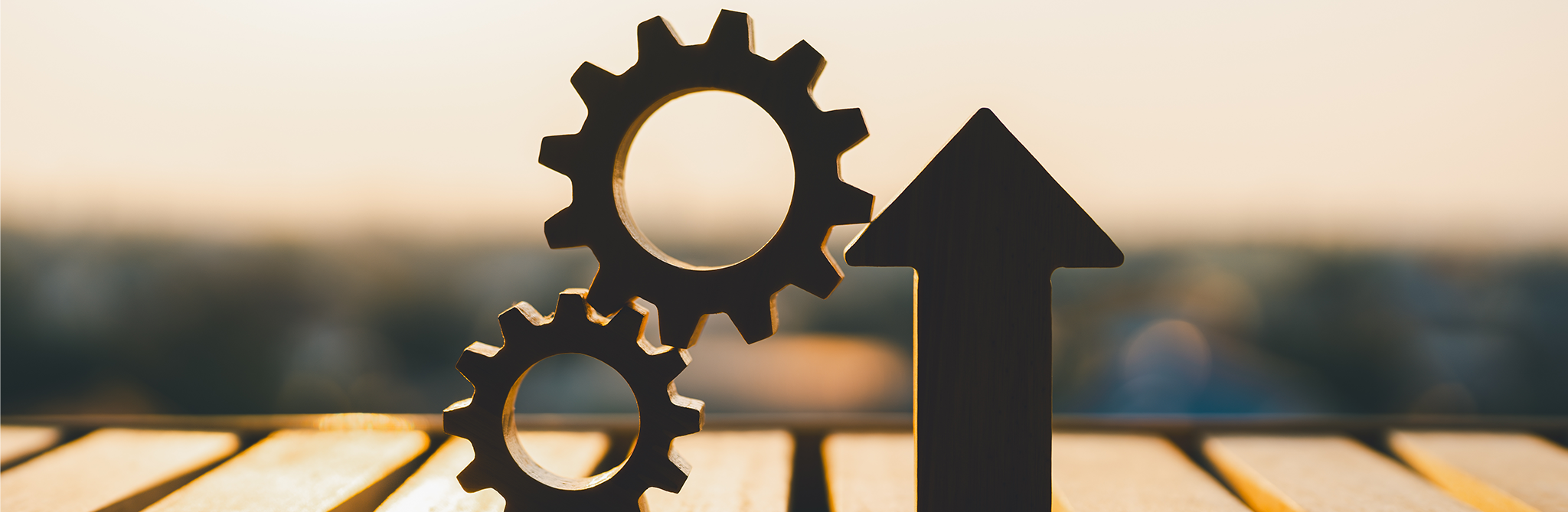 An arrow pointing up next to two cog wheels in sharp focus on a slatted table.