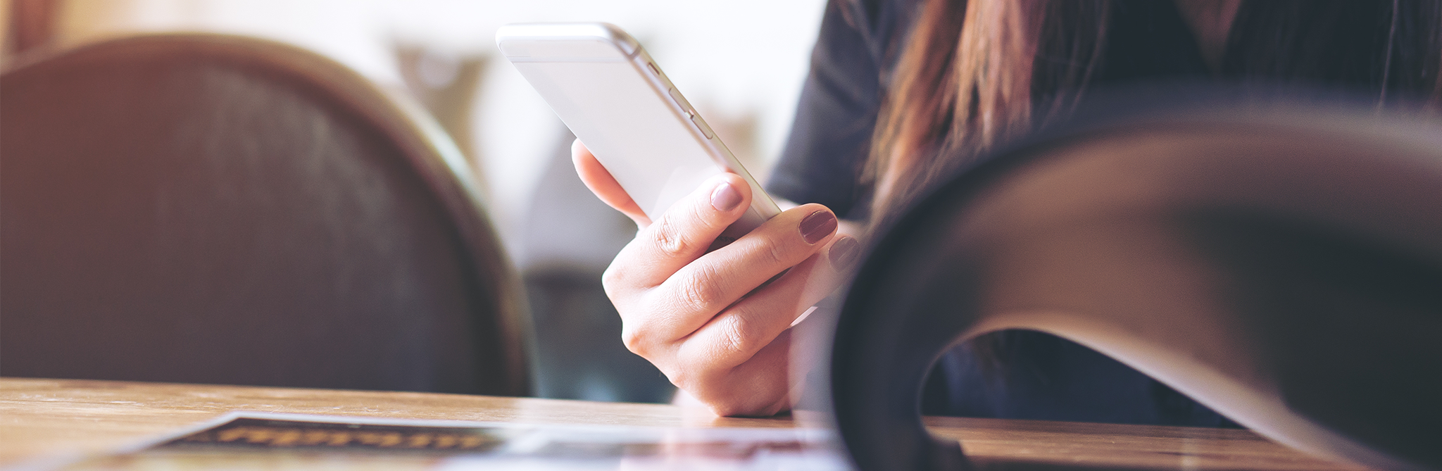 A person with long hair sitting at a table, looking at their cell phone.
