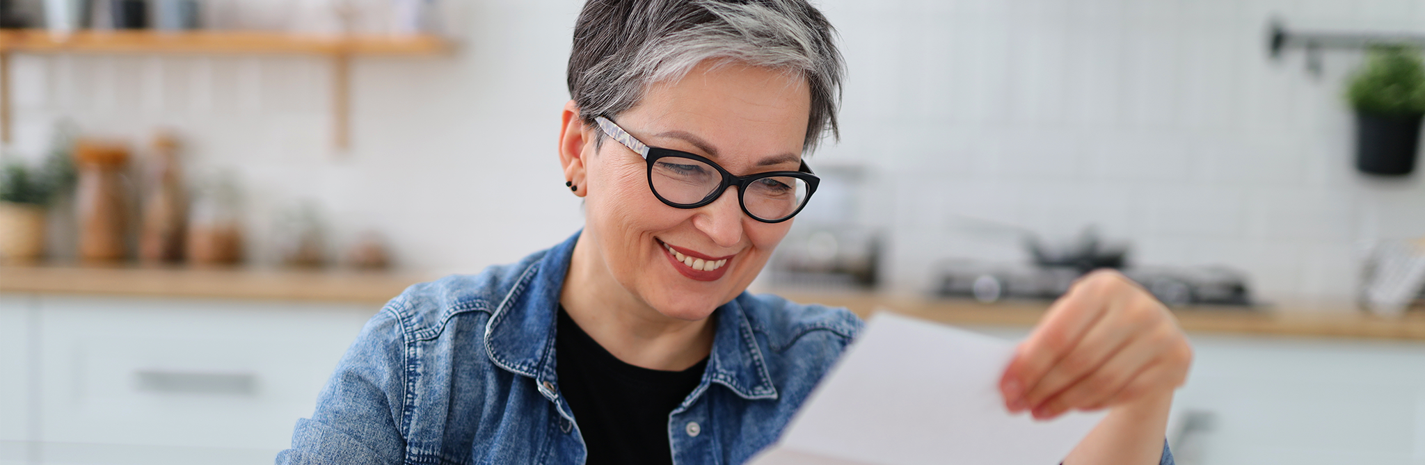 A woman with short salt-and-pepper black hair smiling while reading a piece of paper.