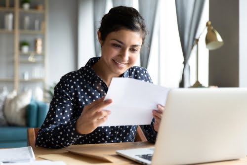 women reading letter at desk in front of laptop.