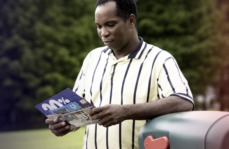 Man looking at direct mail near mailbox