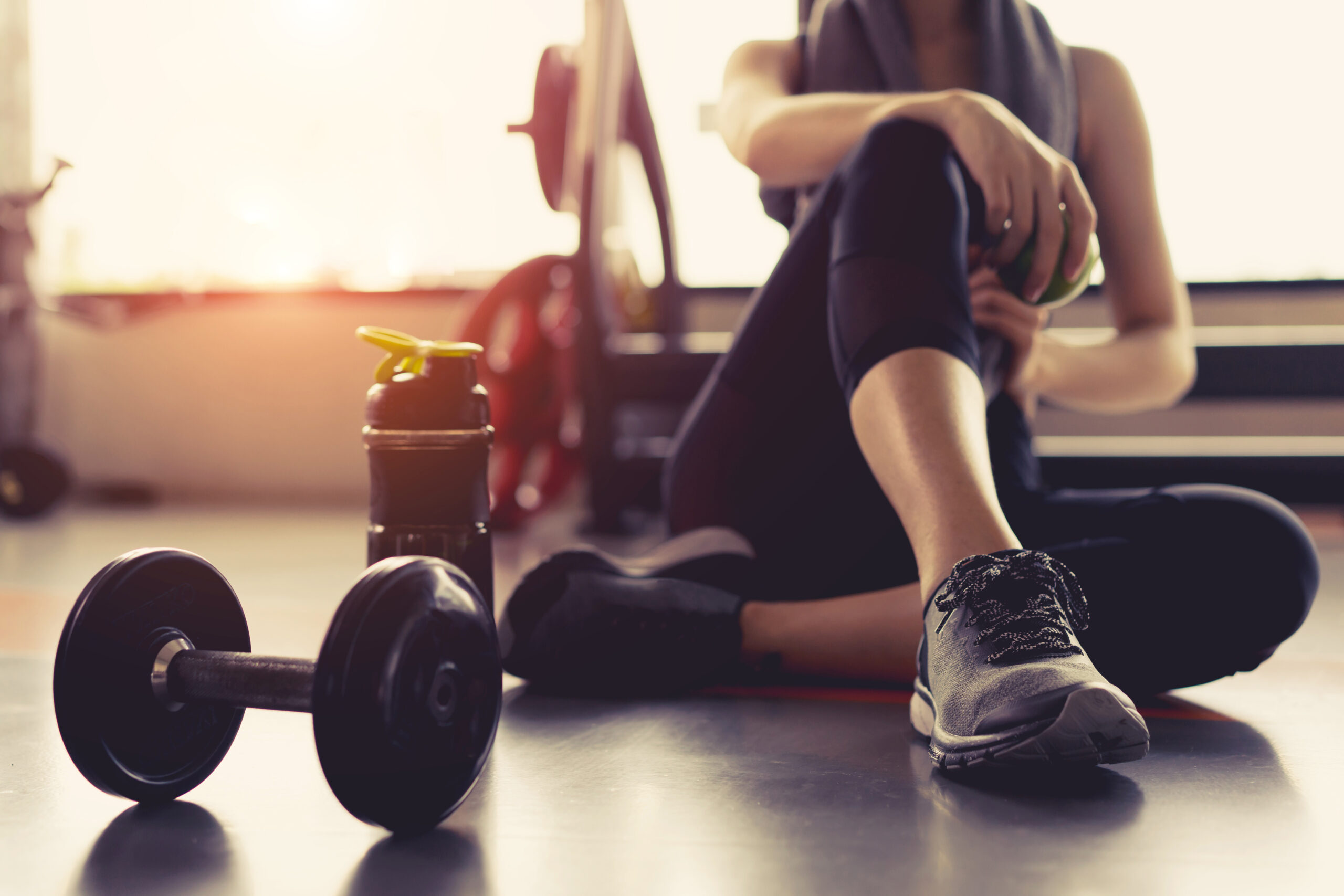 Women sitting in a gym with her legs crossed taking a break.