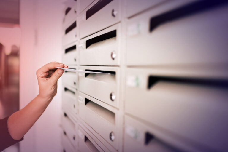 A persons hand putting an envelope in a mail slot.