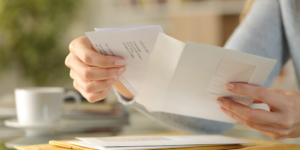Close-up of a woman's hands opening an envelope on a desk at home