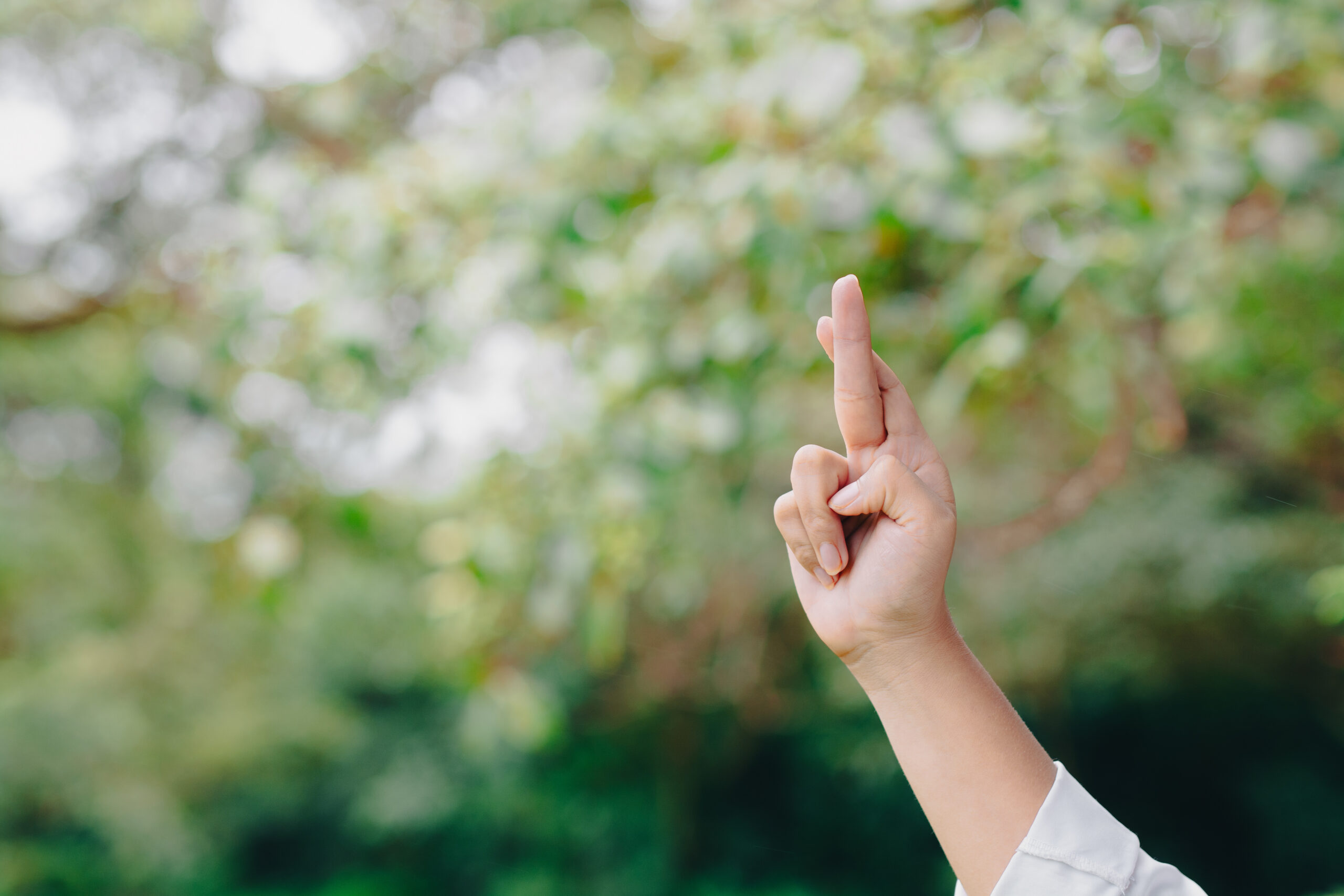 Hand with crossed fingers gesture symbolizing hope and good luck against natural green background