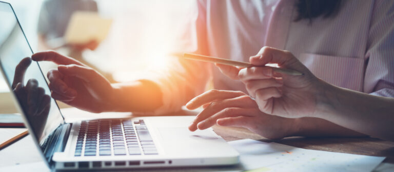 Digital team working on a project in big office. Two women discussing marketing plan. Laptop and paperwork on the table. Indoors